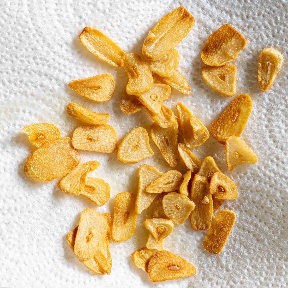 Fried garlic chips cooling on a paper towel.