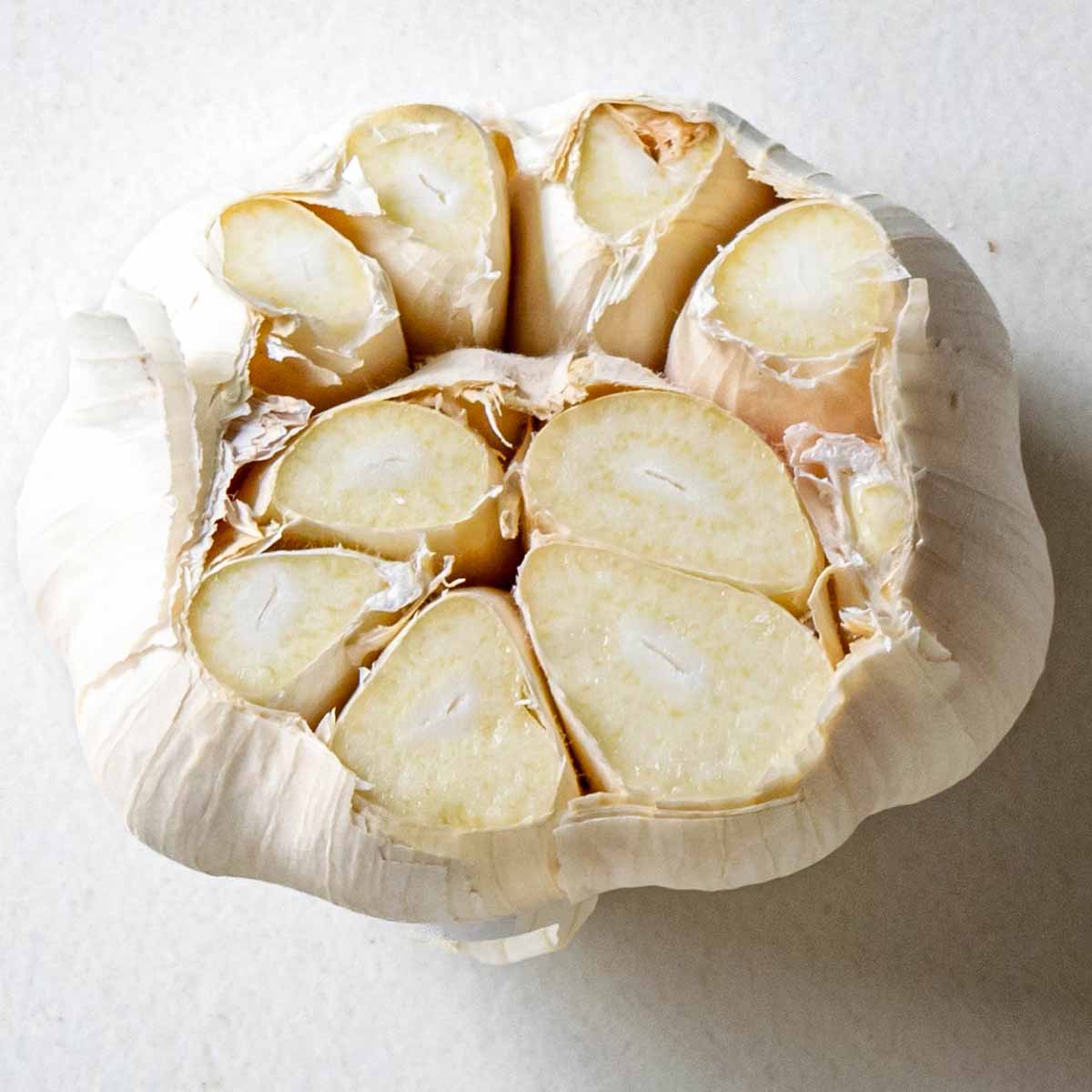 A whole head of garlic with the top cut off to expose the cloves before adding it to the soup pot to simmer.