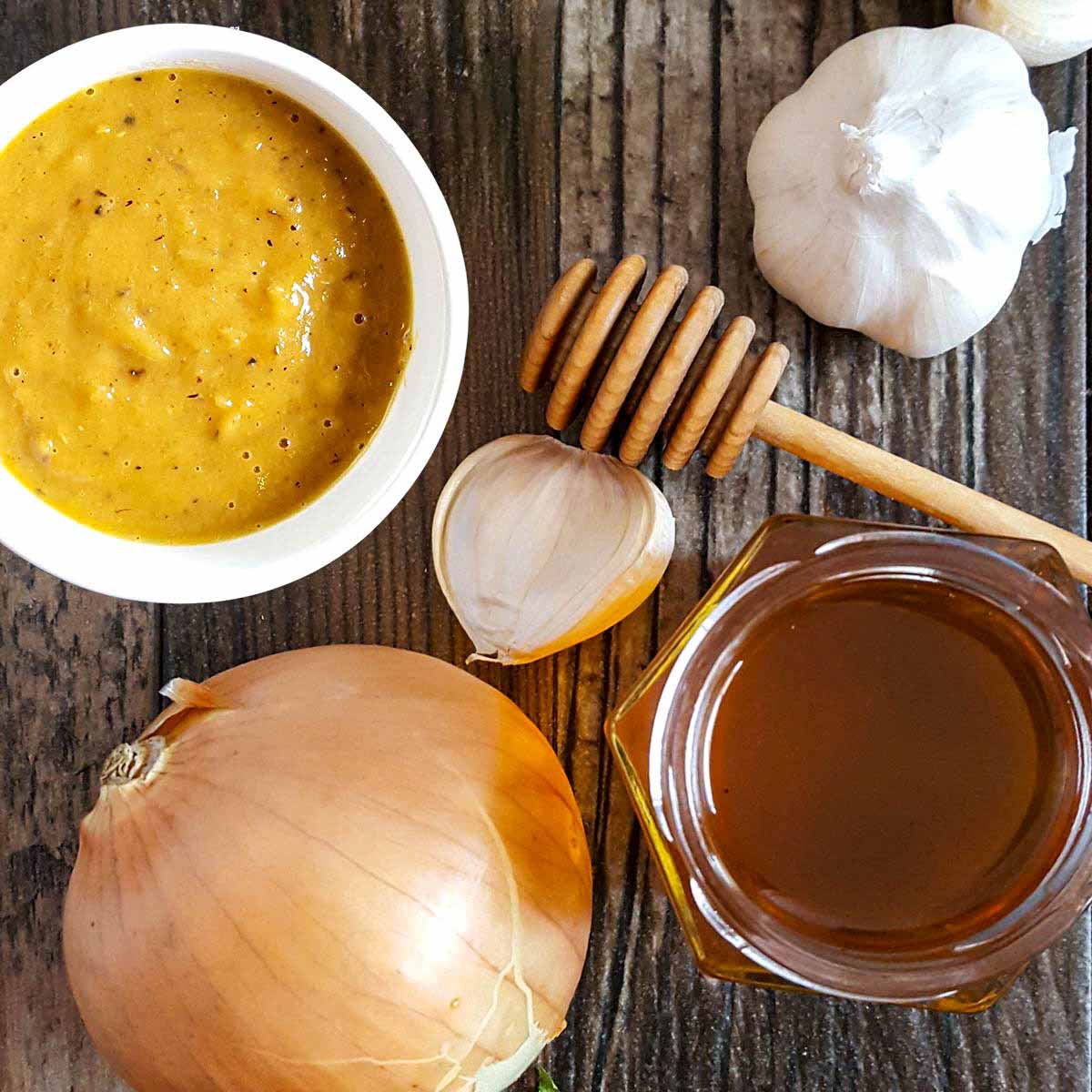 Sweet onion dressing with ingredients on a table top, including garlic, a Vidalia onion, and honey.