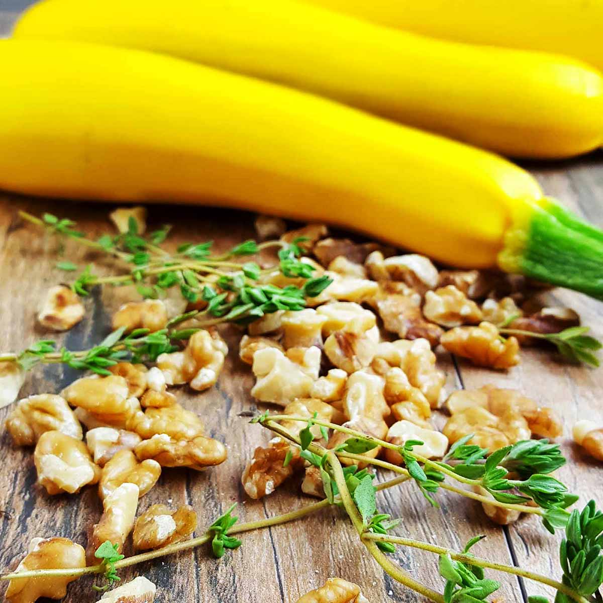 Yellow squash soup ingredients on a table, including fresh yellow squash, walnuts, and thyme