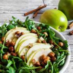 Apple arugula salad with chickpeas, on a plate next to some apples.