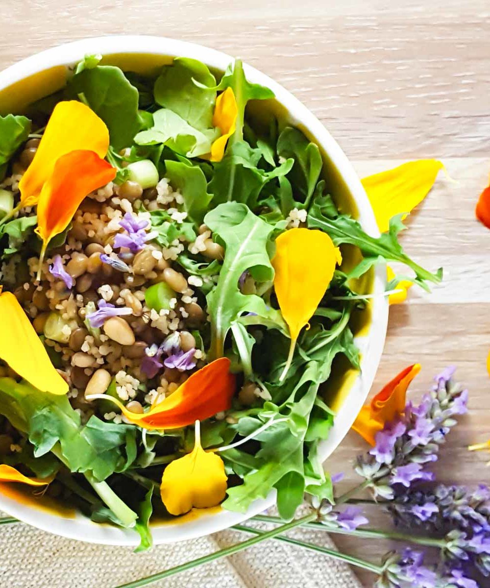 A salad bowl with arugula, lentils, and scattered edible flowers
