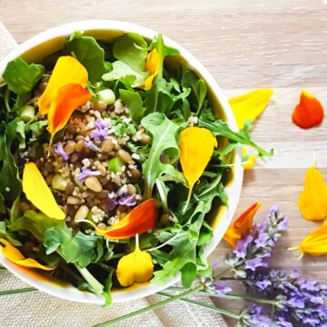 A salad bowl with arugula, lentils, and scattered edible flowers