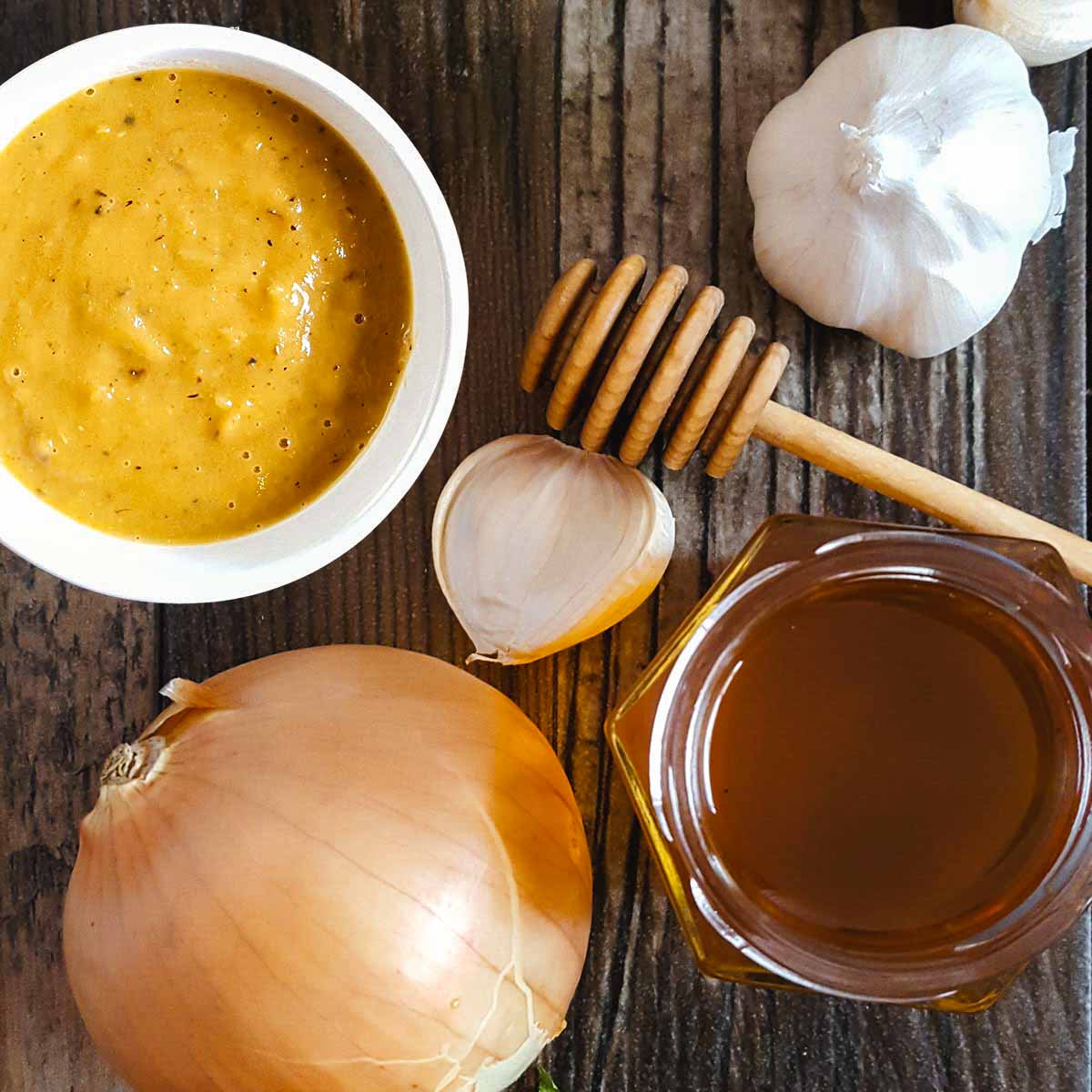 sweet onion sauce on a table with a whole onion, garlic, and honey