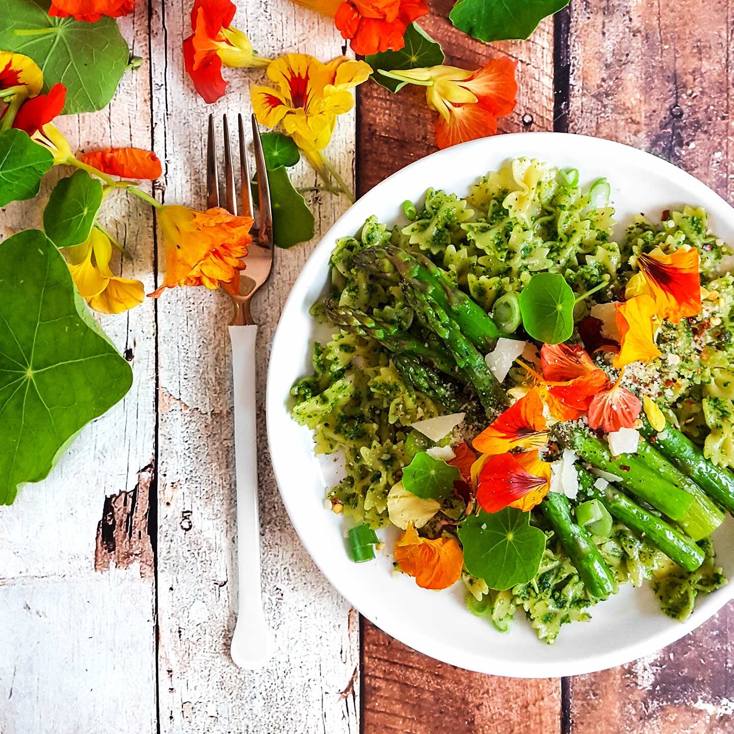 Plate of pasta with asparagus and nasturtium leaves and flowers on the table