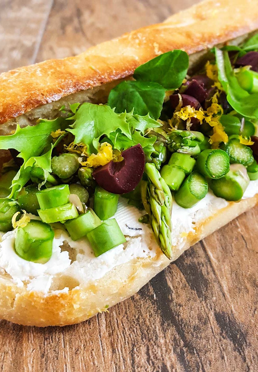 Baguette roll with sliced asapragus, goat cheese, olives, and lettuce