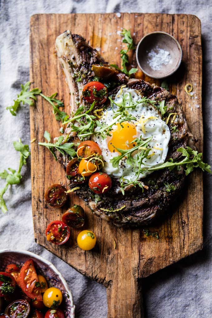 Steak topped with an egg and tomatoes, on a cutting board