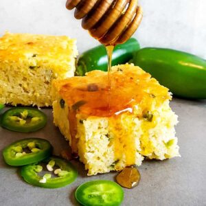 A slice of cornbread drizzled with honey, surrounded by whole and sliced jalapenos