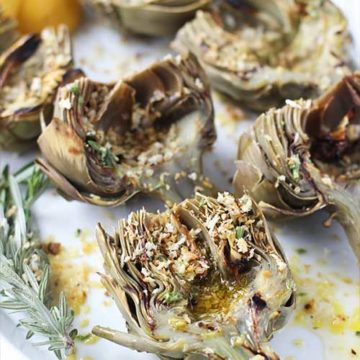 Grilled artichoke halves with breadcrumbs and rosemary sprigs