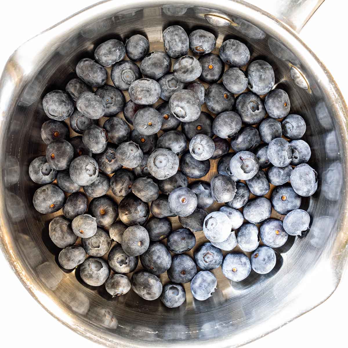 A cup of fresh blueberries in a pan, to be turned into a syrup or compote