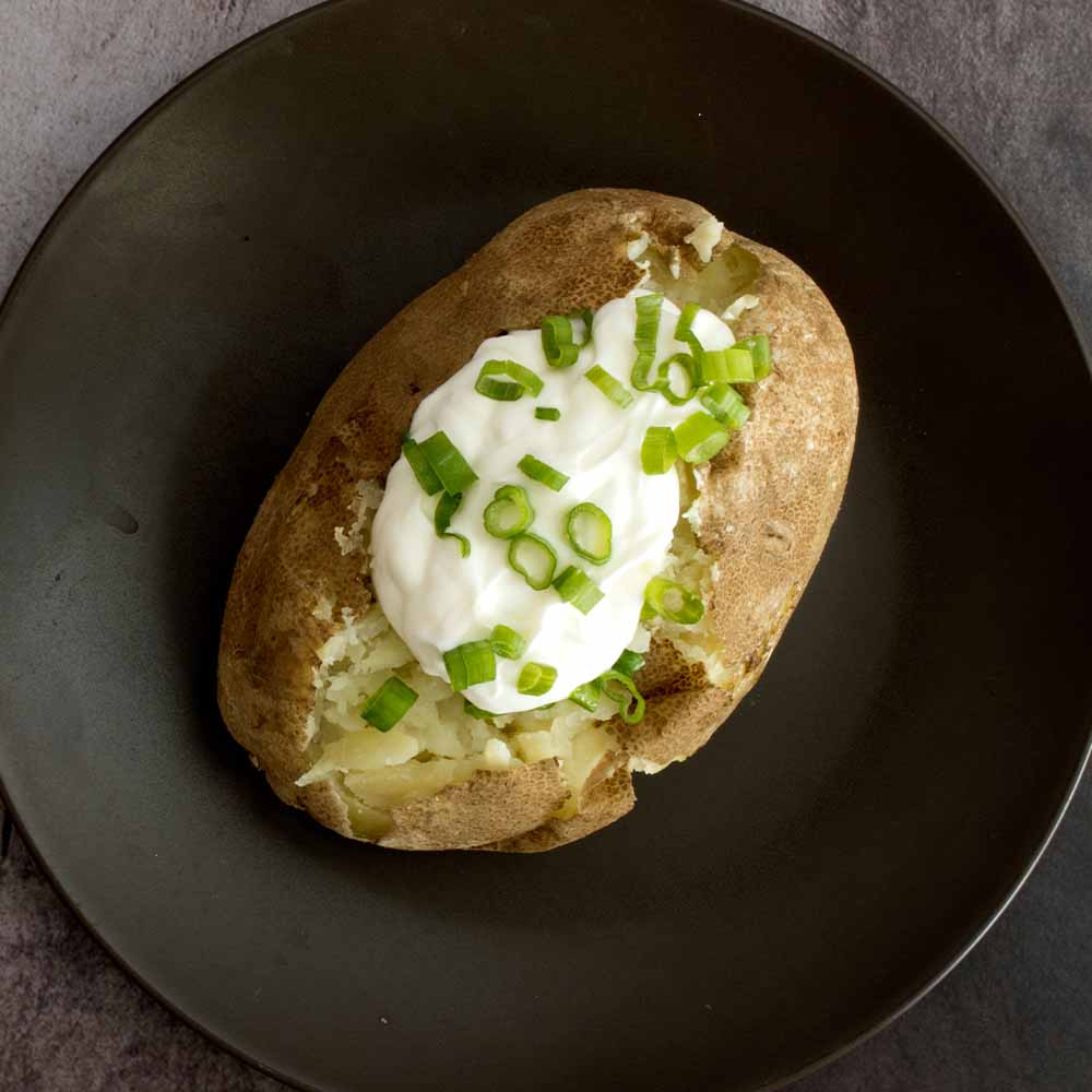A baked potato on a black plate, topped with chives