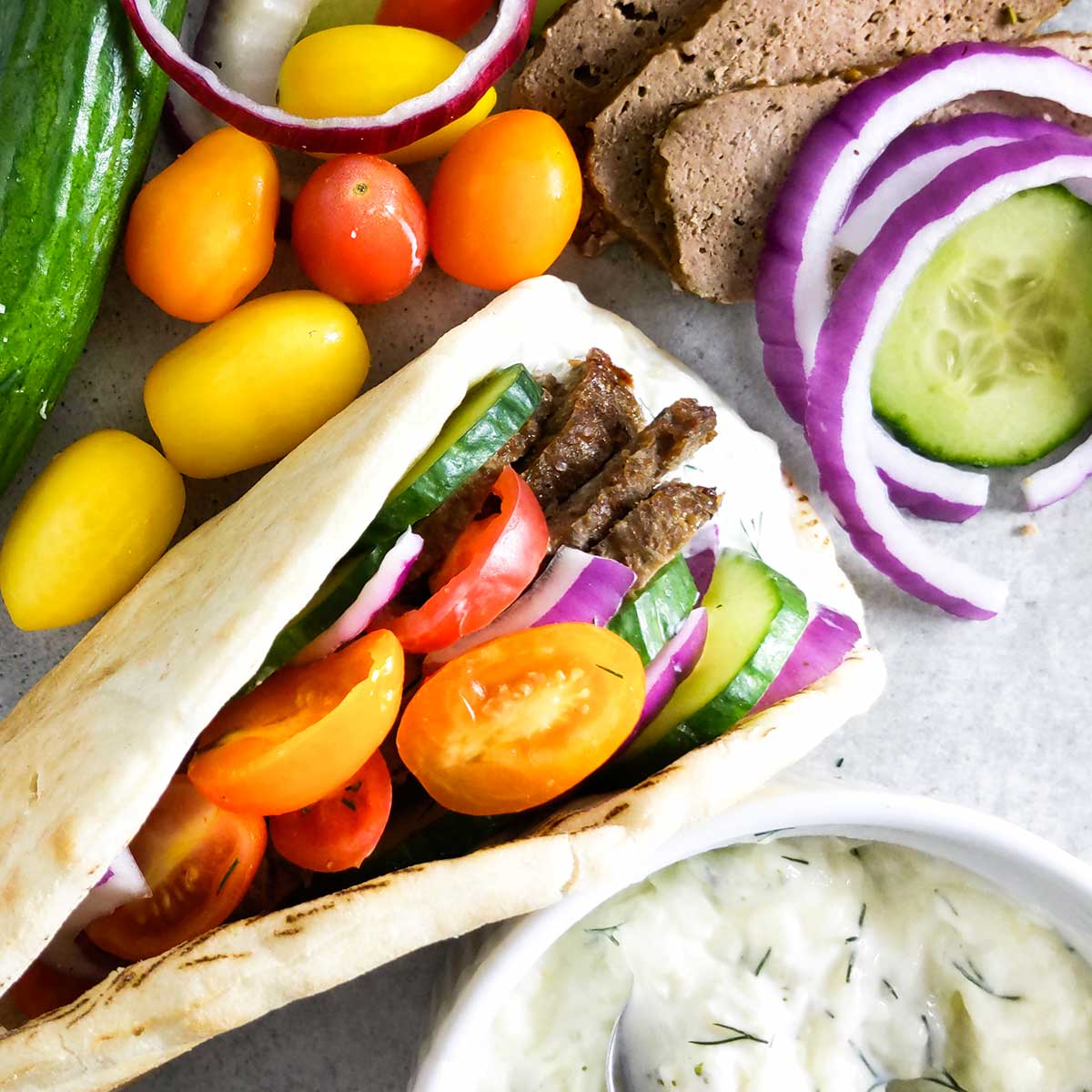 A gyro filled with homemade meat, vegetables, and tzatziki sauce