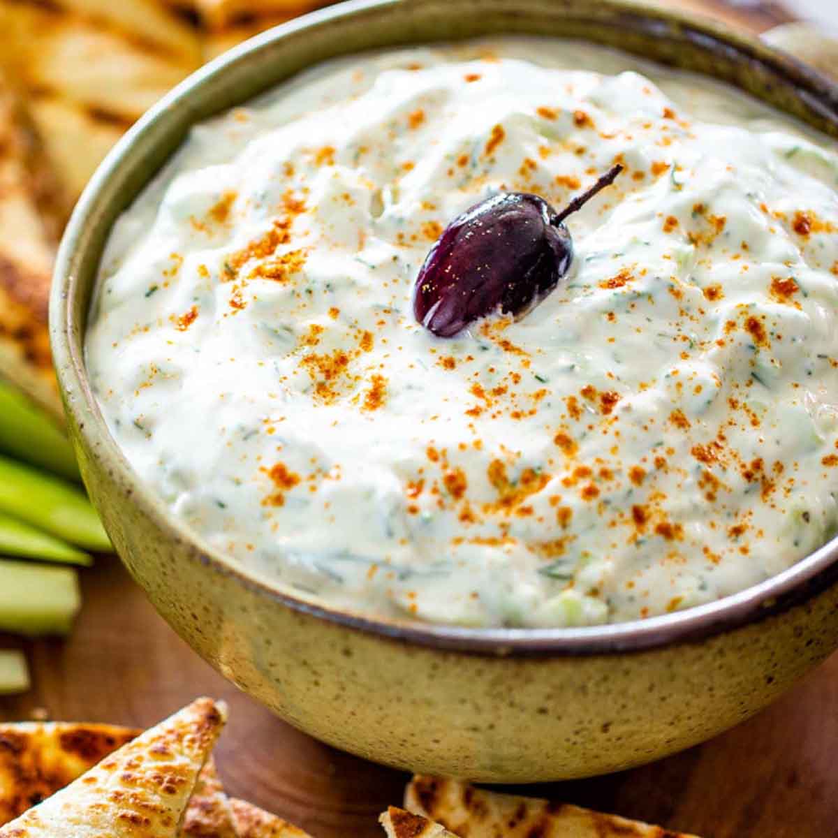 Spicy tzatziki sauce variation in a bowl, surrounded by pitas and vegetables. Recipe from Jo Cooks.
