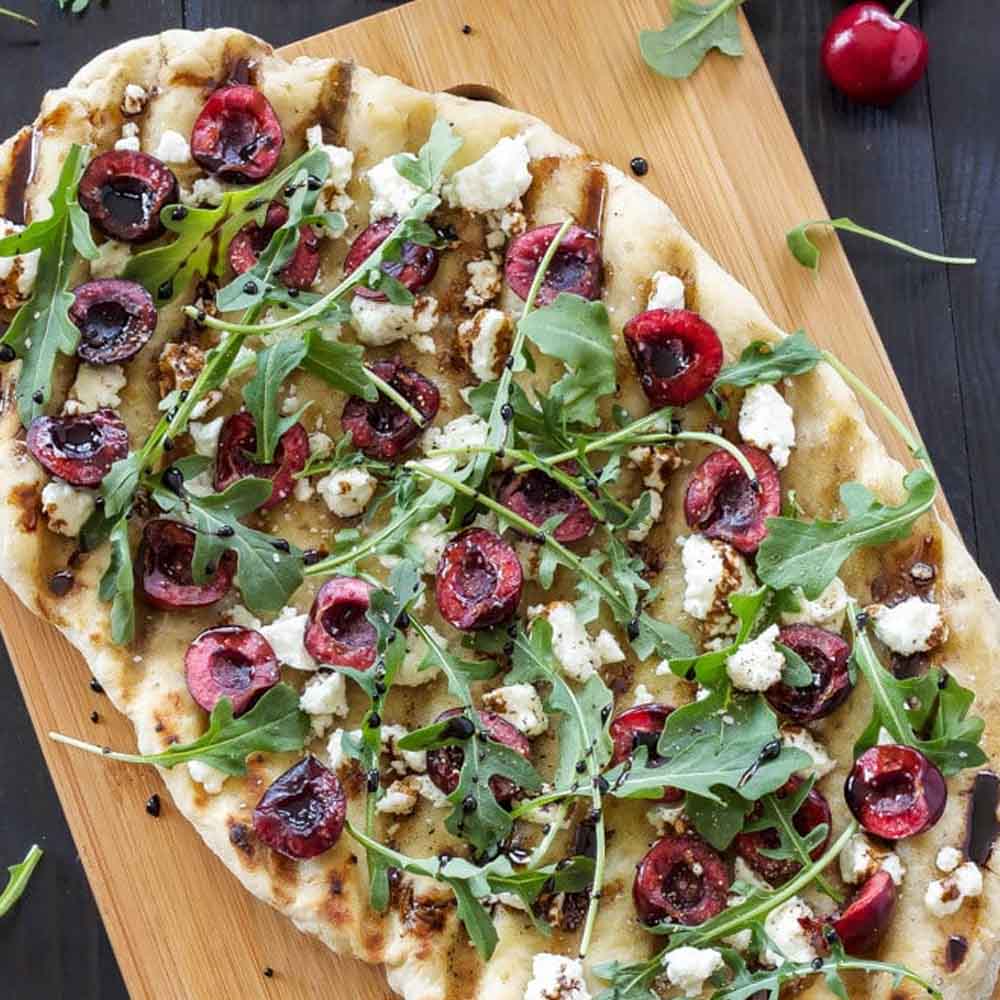 A homemade pizza topped with arugula, goat cheese, and fresh cherries from Recipe Runner