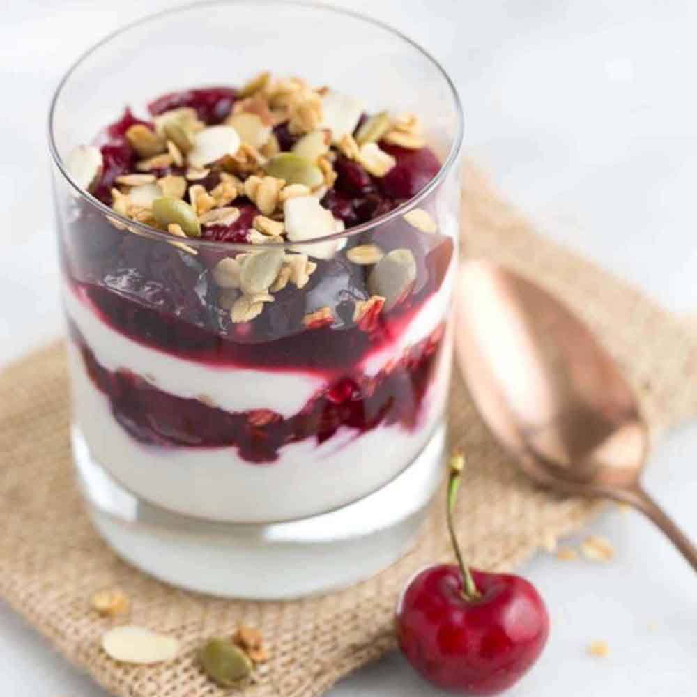 A glass jar with a cherry yogurt parfait topped with a crunchy granola. Recipe from Jessica Gavin.
