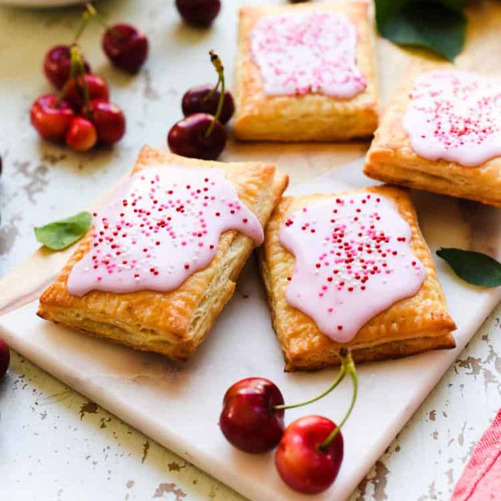Cherry pop tarts with a homemade filling on a table with fresh cherries. Recipe from Kitchen Confidante