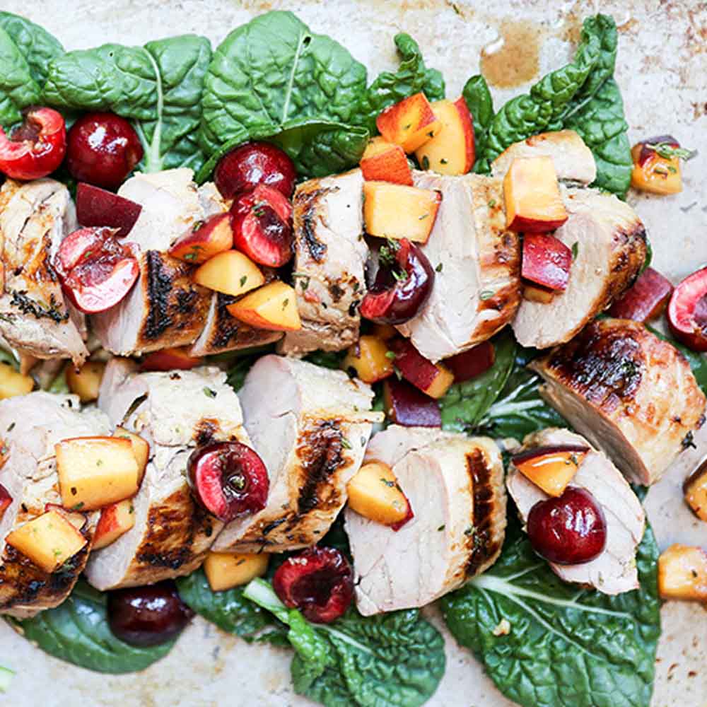 Grilled pork tenderloin, sliced up on a platter, topped with peaches and cherries, recipe from Floating Kitchen
