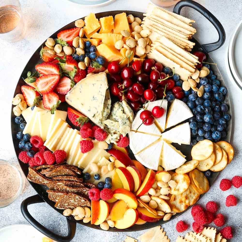 Summer cheese board with various soft and hard cheese, crackers, nuts, and fruit, including strawberries, blueberries, raspberries, peaches, and cherries. Recipe from Damn Delicious.