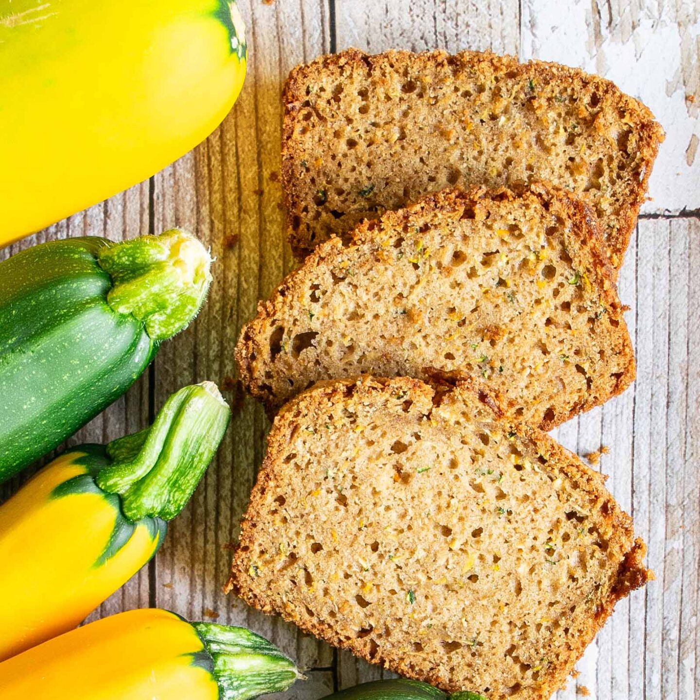 Zucchini bread slices next to zucchini and summer squash to show how easy the recipe is