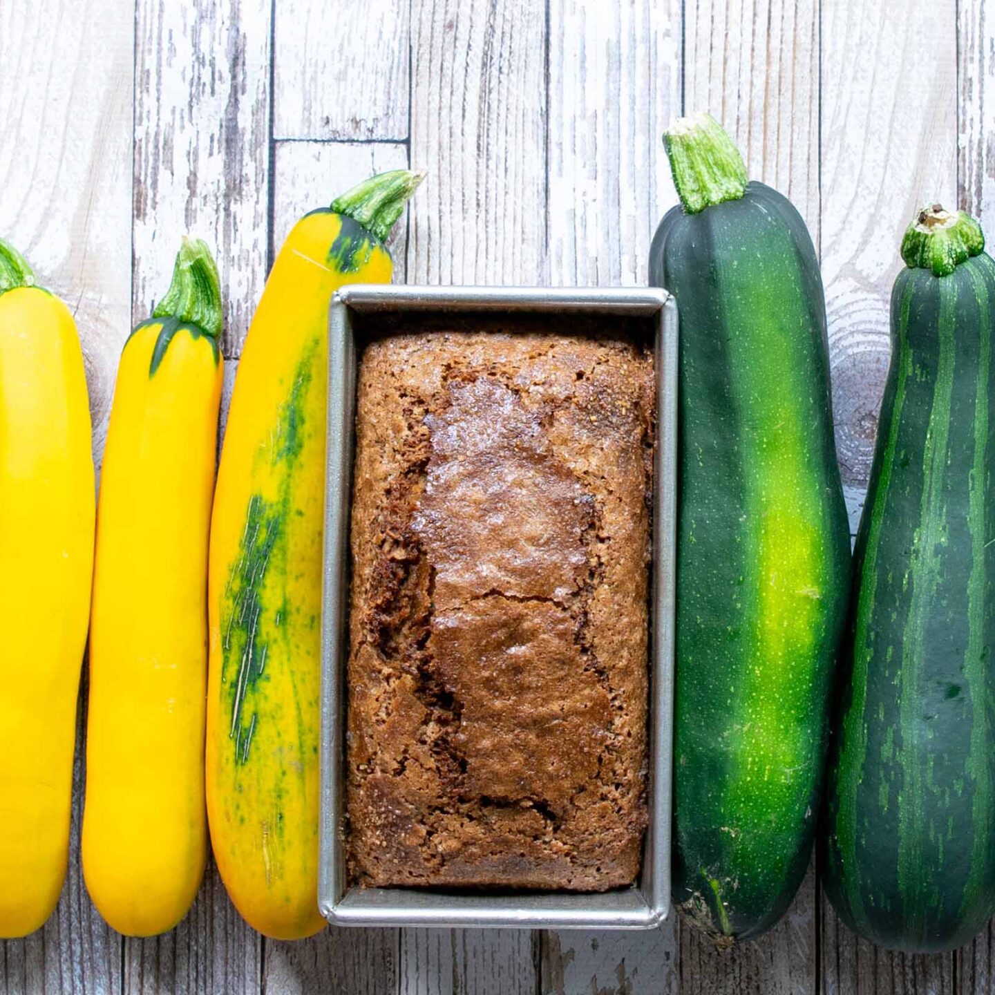 A zucchini bread loaf next to garden zucchini and summer squash