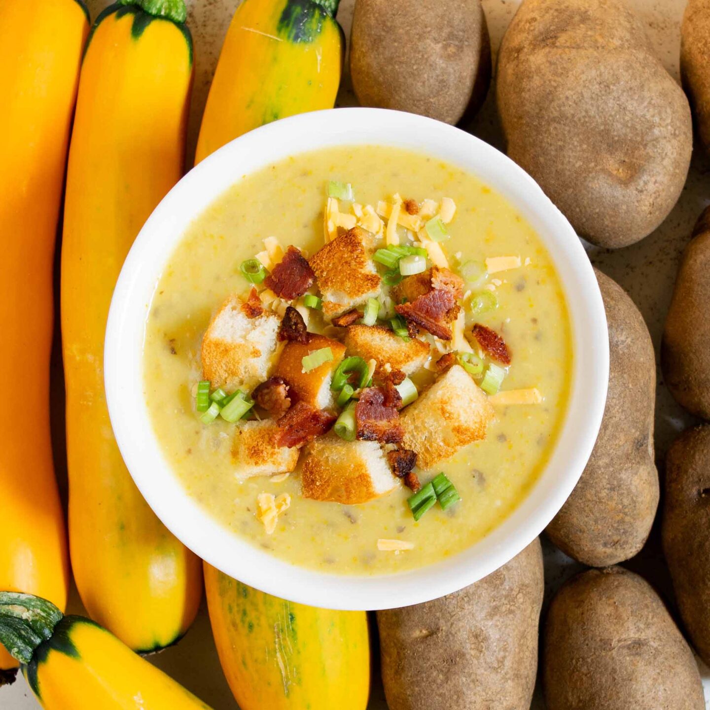 A bowl of loaded potato zucchini soup, topped with bacon, green onions, and croutons.