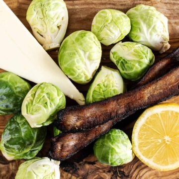 Brussels sprouts with bacon strips, parmesan, and lemons on an olive wood board