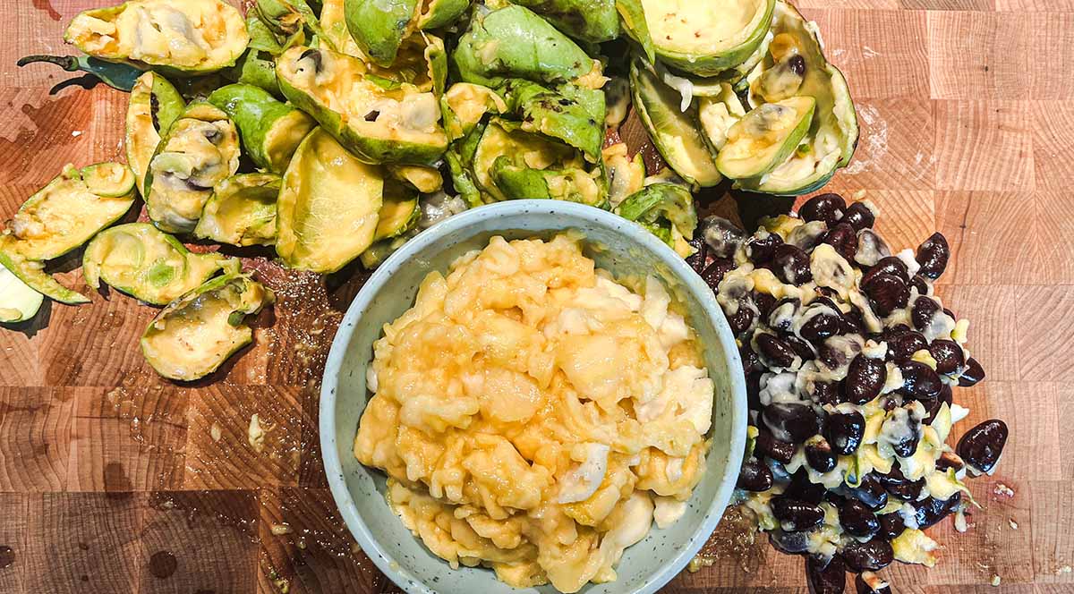 Pawpaw flesh in a bowl, next to a pile of skins and seeds