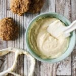 A bowl of pawpaw cream cheese frosting next to a mixer paddle and pawpaw cookies.