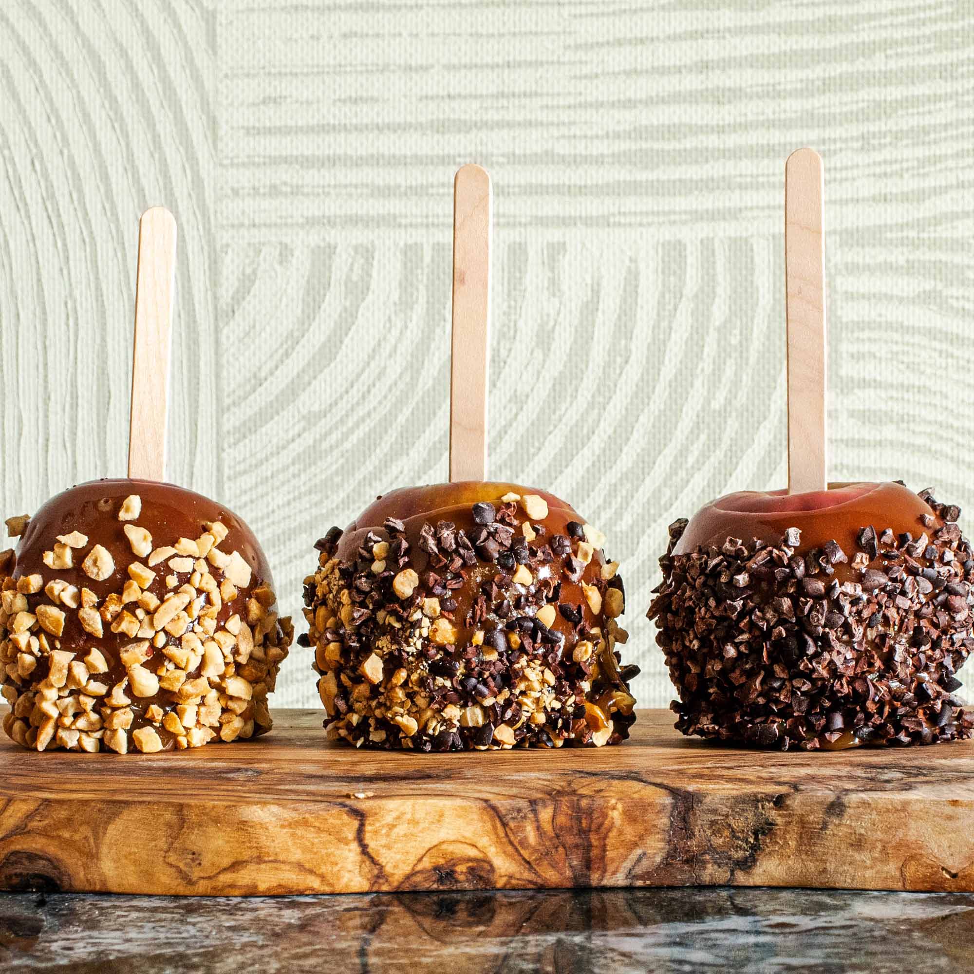 3 homemade caramel apples with different toppings: nuts, peanuts & chocolate, and chopped chocolate.