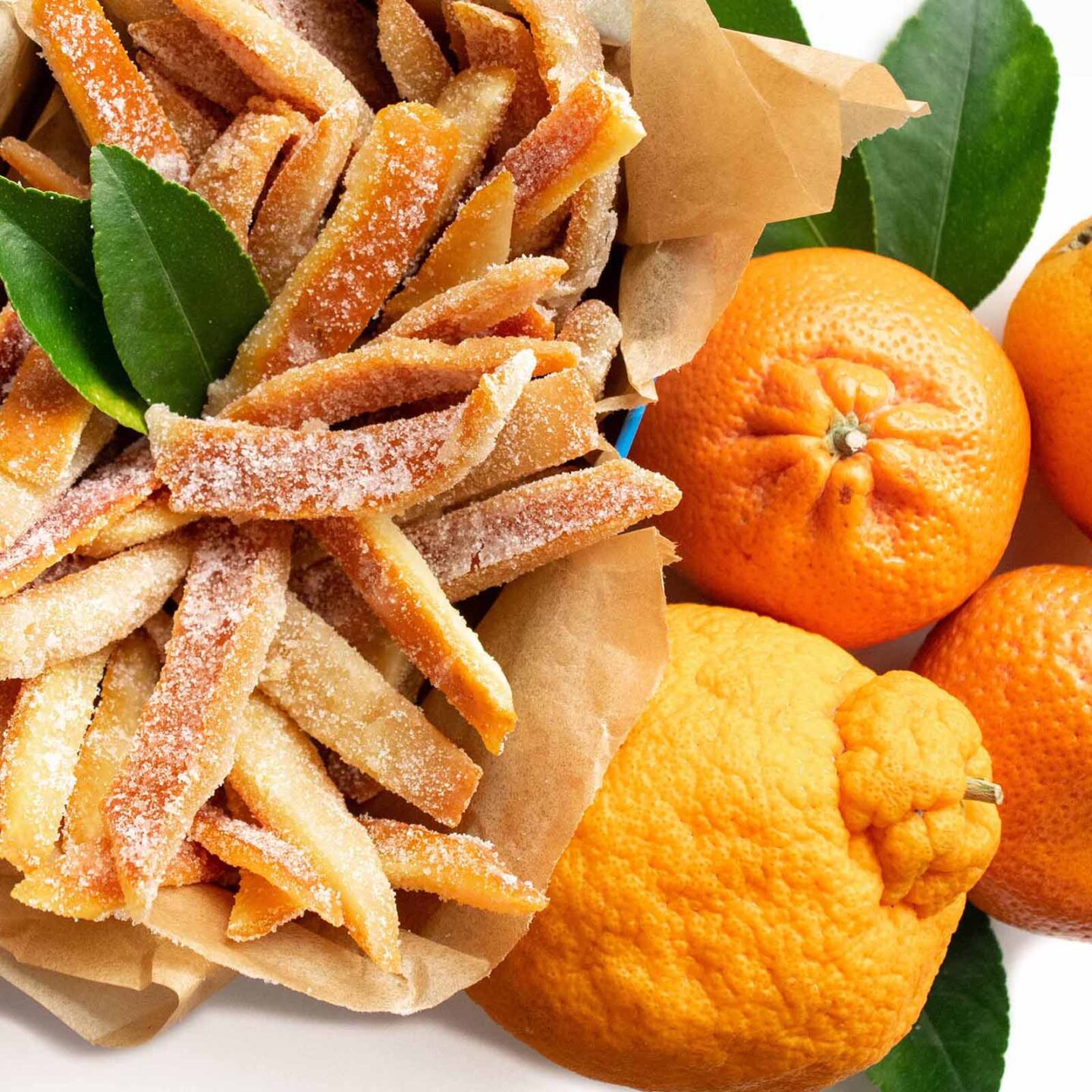 Candied orange peels in a basket next to fresh oranges