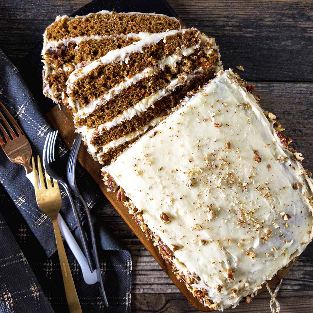 A layered carrot cake without raisins, topped with cream cheese frosting and nuts. It's sitting on a table set for Easter or St. Patrick's day.