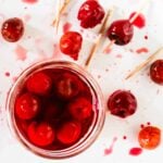 A jar of homemade maraschino cocktail cherries with a few cherries and toothpicks on a table
