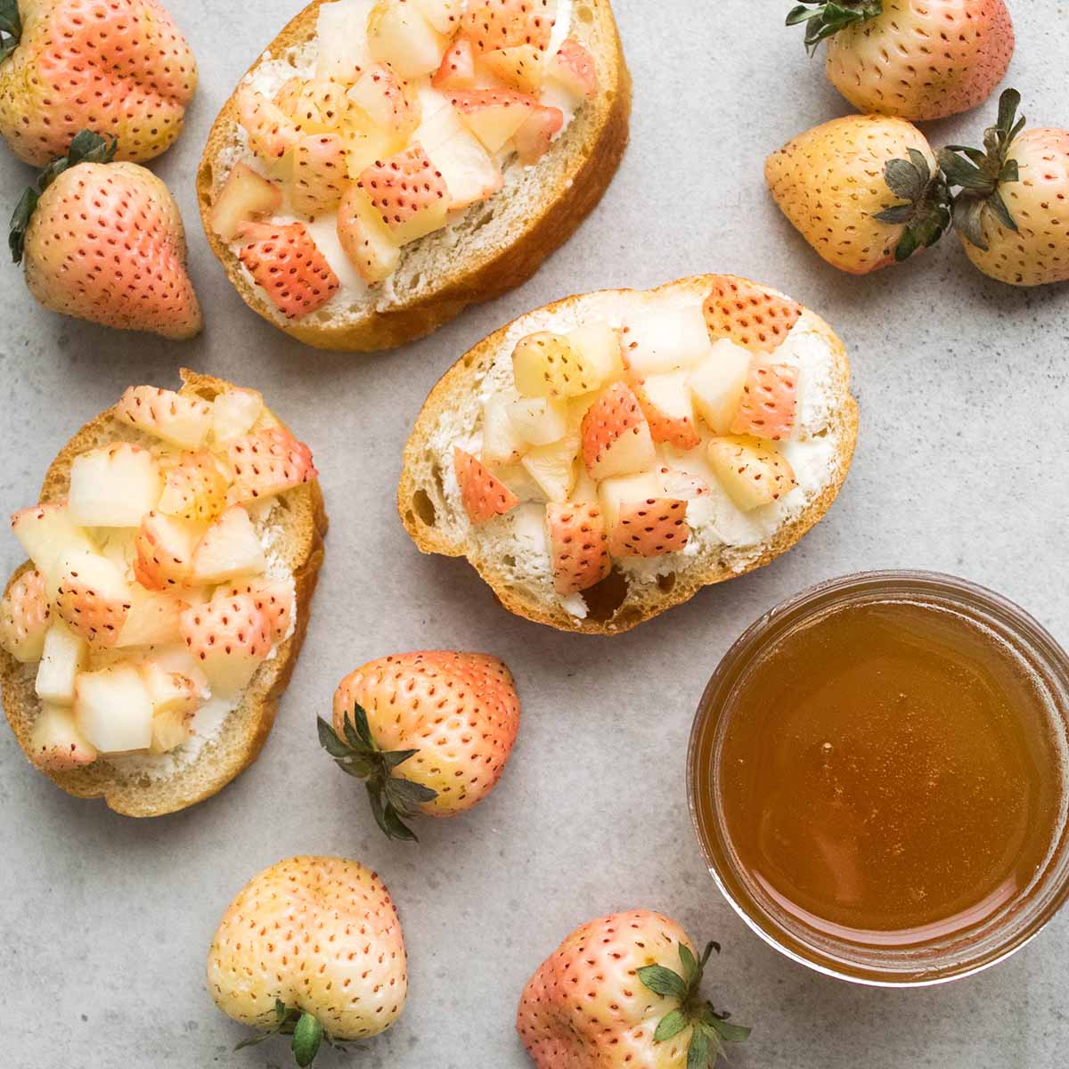 Pineberry bruschetta (crosini) appetizer toasts with goat cheese and honey, on a gray tabletop