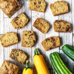 Mini zucchini bread loaves on a table next to fresh zucchini