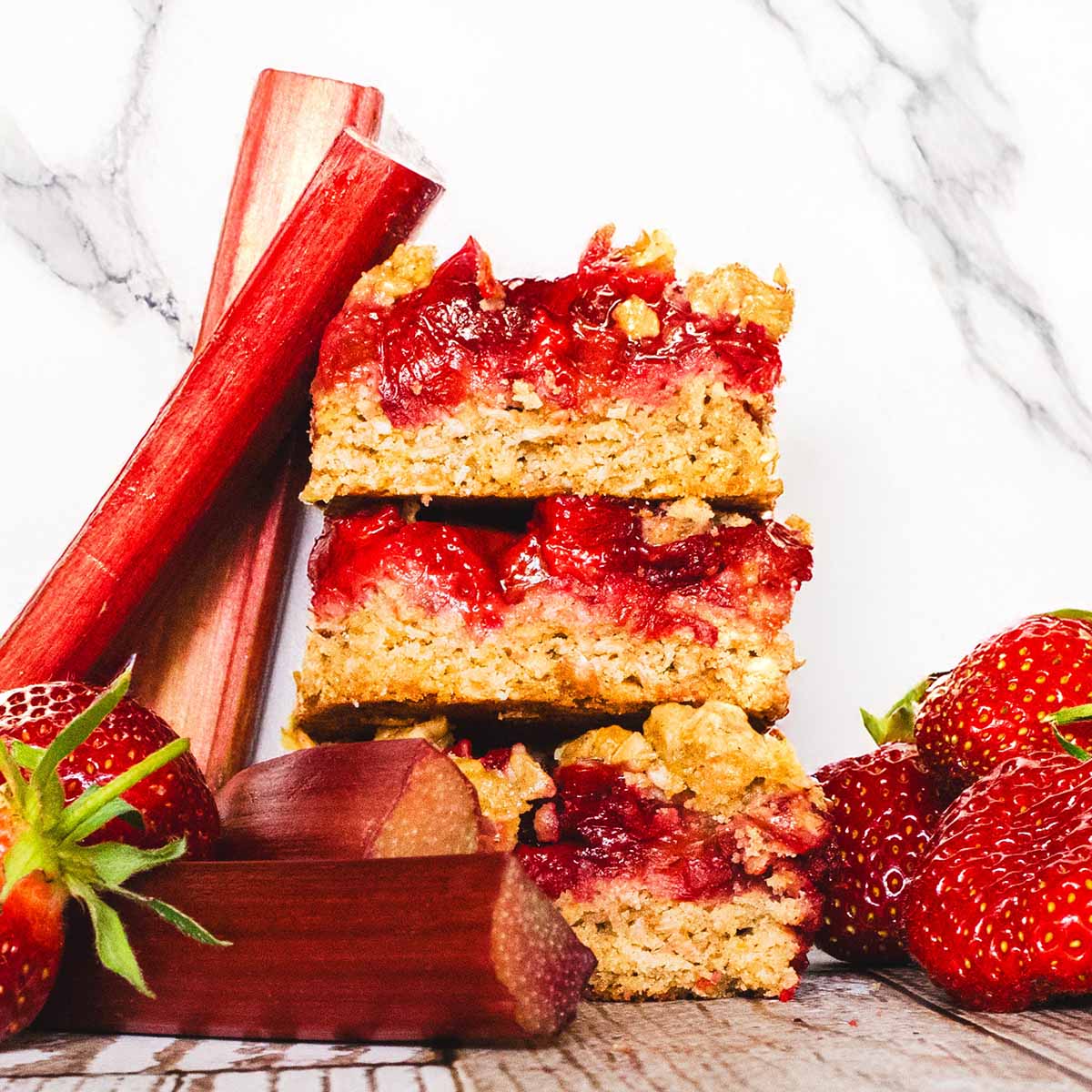 Strawberry rhubarb bars with fresh rhubarb and strawberries in the foreground