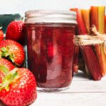 A jar of strawberry rhubarb jam made without pectin, next to fresh strawberries and rhubarb stalks