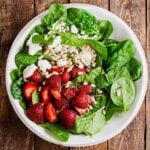 A strawberry spinach salad with feta on a plate, on a summer picnic table