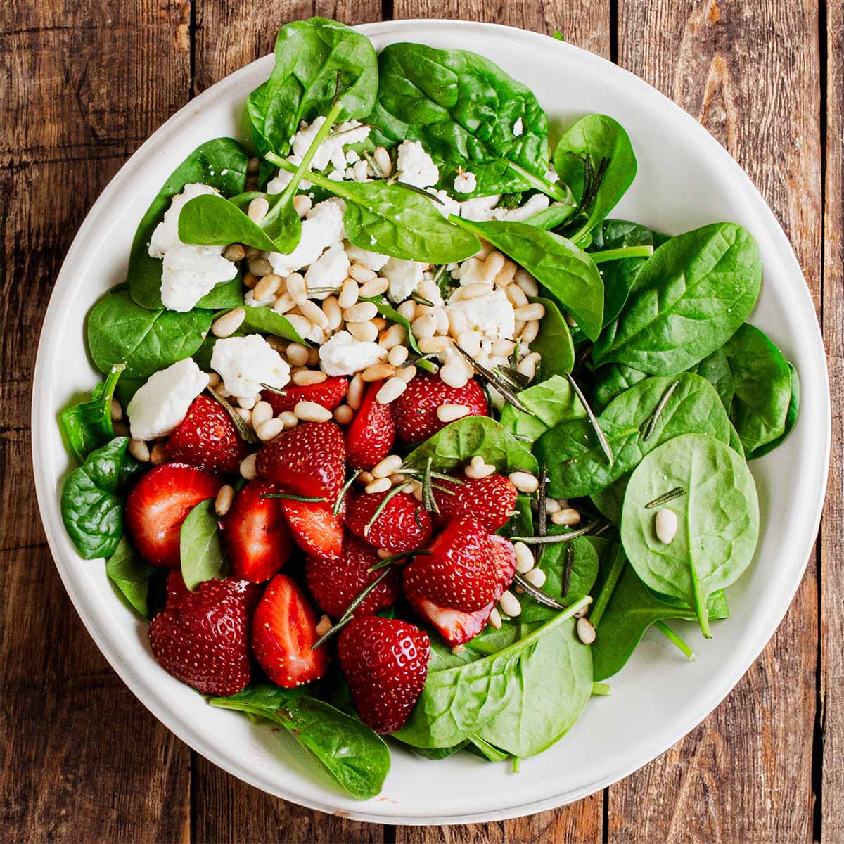 A strawberry spinach salad with feta on a plate, on a summer picnic table