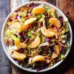 A dinner plate filled with Chinese chicken salad, mandarin oranges, shredded cabbage, and a sesame salad dressing.