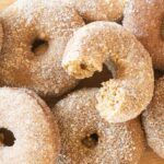 A pile of baked apple cider donuts with one cut in half to show the texture