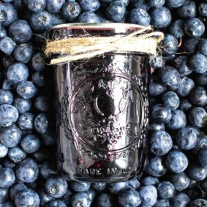 Blueberry syrup in a jar, on top of a pile of fresh blueberries.