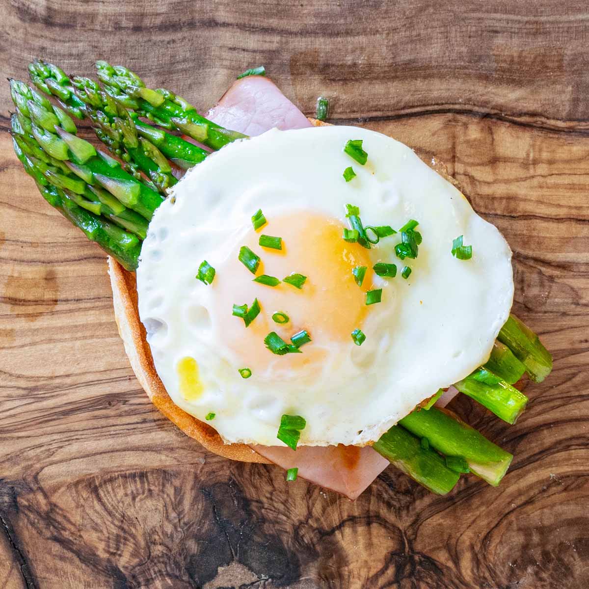 Eggs Benedict with asparagus, deli ham, and a fried over easy egg that was easy and quick to make. Set on a wood cutting board backdrop.