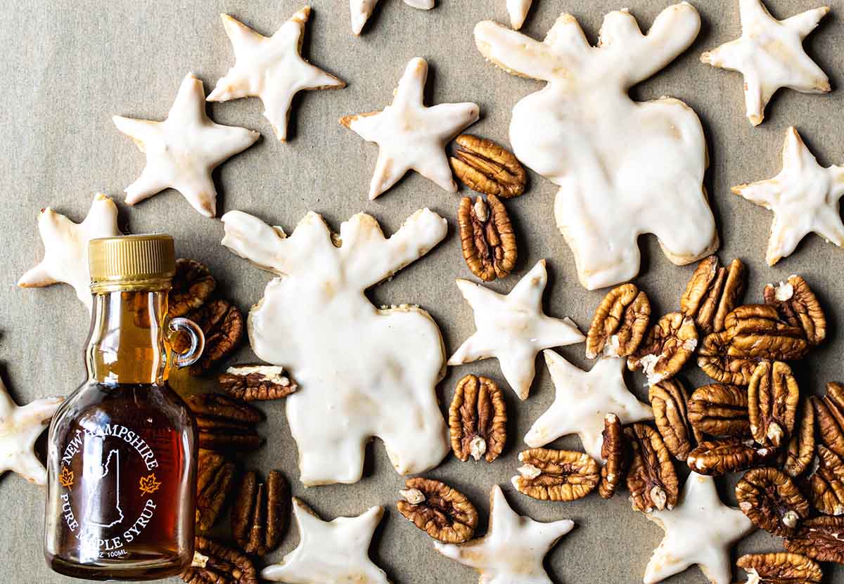 Maple pecan cookies with a bottle of maple syrup and a pile of fresh pecans