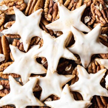 Maple pecan cookies cut out in a star shape for Christmas, on top of a pile of fresh pecans