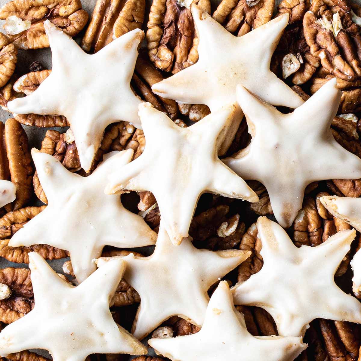 Maple pecan cookies cut out in a star shape for Christmas, on top of a pile of fresh pecans