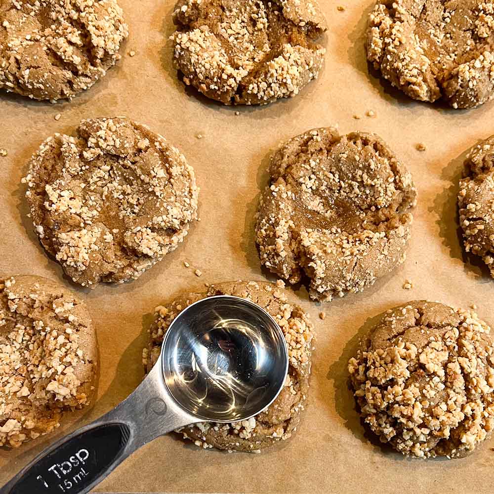 A tray of peanut butter blossoms and chopped nuts, with a tablespoon to make the indent for the chocolate ganache center, which replaces the Hershey Kiss.