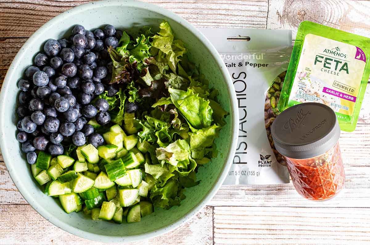 A large bowl of blueberry cucumber salad to bring to a picnic or bbq to feed a crowd, with other ingredients on the side.