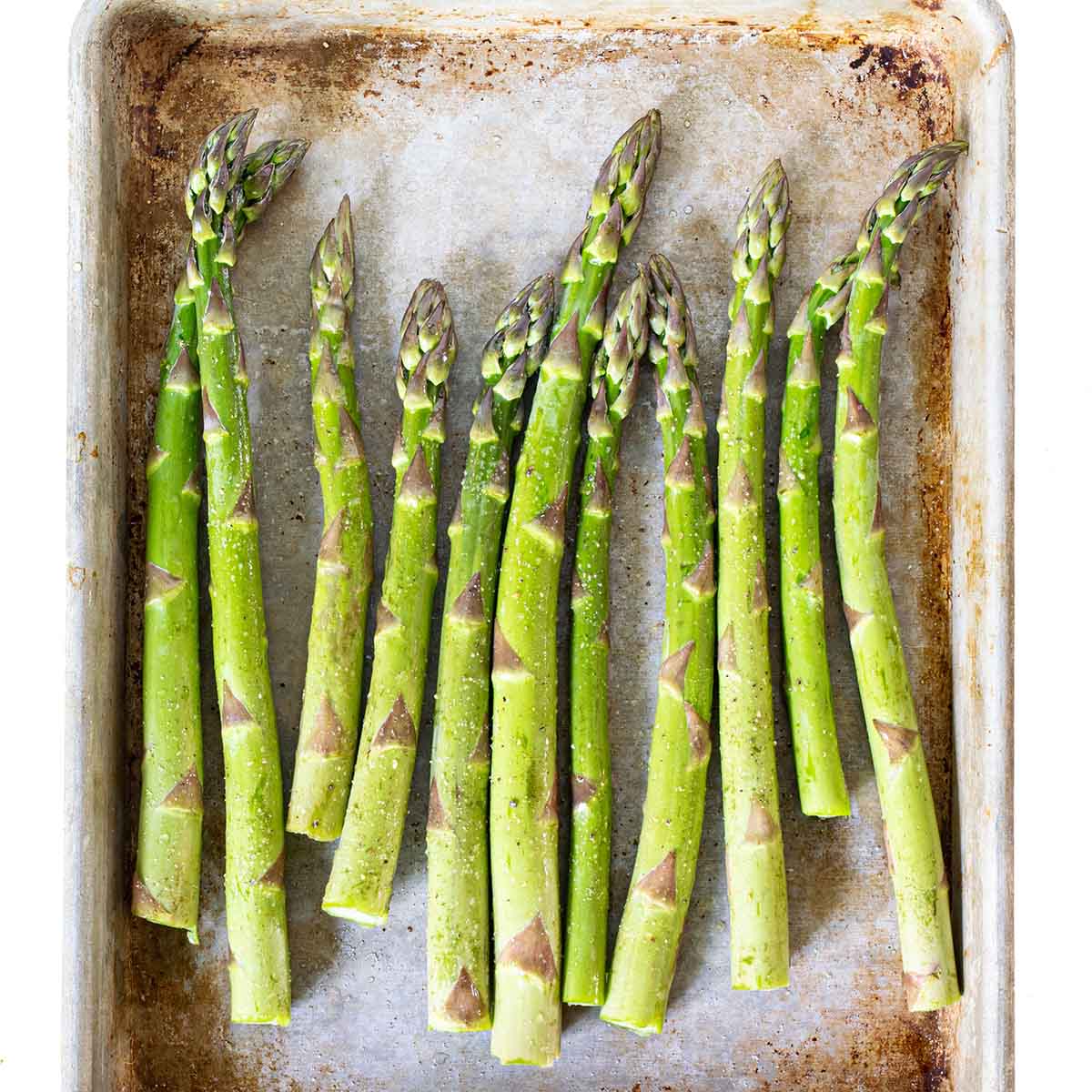 Asparagus on a tray, ready to roast with olive oil, salt, and pepper