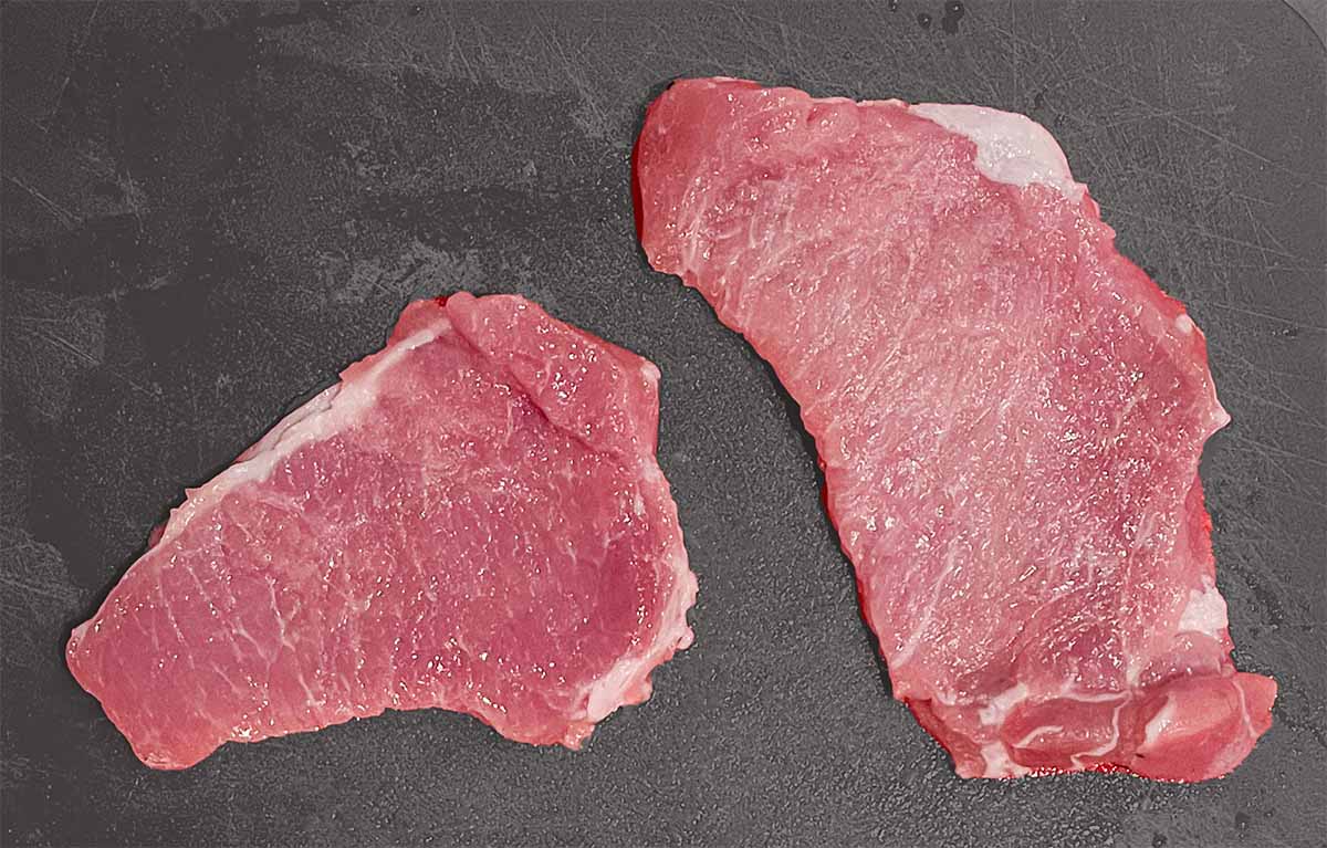 2 raw pork chops on a gray cutting board, before pan frying in a skillet
