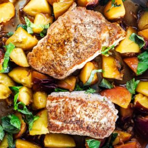 2 boneless pork chops in a skillet with a sauce of peaches, ginger, brown sugar, and basil